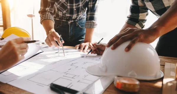 stock image Engineer teams working together at table with blueprint plan and building helmets hardhat  