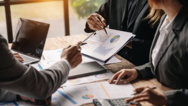 Ekonomik durumu ve mali durumu analiz eden bir iş ekibi. İnsanlar ellerinde kağıt ve grafiklerle masada oturuyorlar. 