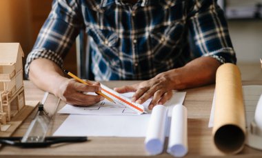 İşadamı el işi ve dizüstü bilgisayarla ofisteki inşaat alanında mimari proje üzerinde çalışıyor.