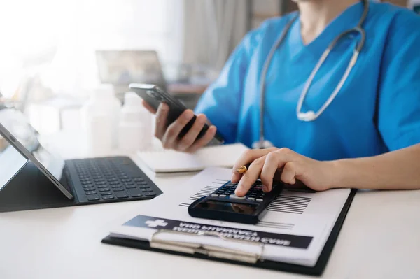 Healthcare costs and fees concept.Hands of smart doctor used a calculator and smartphone, tablet for medical costs at hospital in morning light