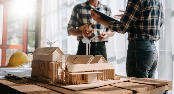 Close up shot of scale model house on table with architects. Two architects making architectural model in office together. to form a new building