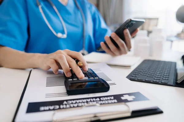 Healthcare costs and fees concept.Hands of smart doctor used a calculator and smartphone, tablet for medical costs at hospital in morning light