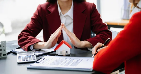 Female real estate agent is use hands to protect red roof for the concept of real estate investment about house trading, purchase at  the desk in office