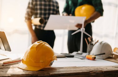 Engineer desk with object paper and tablet with blurry engineer teamwork hardworking to consults about their building project. in sun light