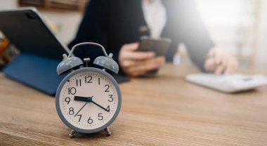 Masadaki çalar saat. Ofis binasında ya da gece evde dizüstü bilgisayar kullanarak çalışan bir iş kadını. ve akıllı telefon.