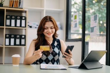 businesswoman  using smart phone, tablet payments and holding credit card online shopping, omni channel, digital tablet docking keyboard computer at office in sunlight