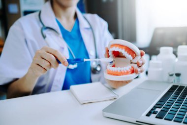 Dentist sitting at table with jaw samples tooth model and working with tablet and laptop in dental office professional dental clinic. Medical doctor working