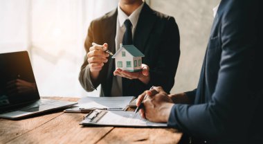 Real estate broker agent presenting and consult to customer to decision-making sign insurance form agreement, home model, concerning mortgage loan offer 