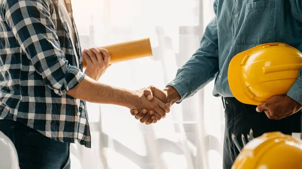 Construction team shake hands greeting start new project plan behind yellow helmet on desk in modern office center to consults about their building project