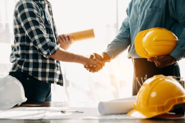 Construction team shake hands greeting start new project plan behind yellow helmet on desk in modern office center to consults about their building project