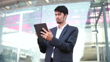 Başarılı iş adamı, ofisin yakınındaki açık havada, tablet bilgisayarda çalışıyor. 