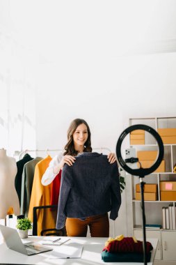 Fashion blogger concept, Young woman selling clothes on video streaming.Startup small business SME, using smartphone or tablet taking receive and checking in home office
