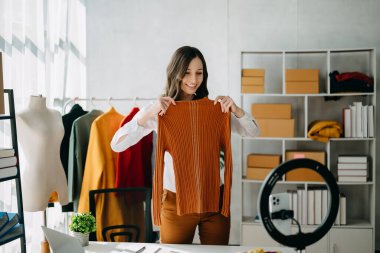 Fashion blogger concept, Young woman selling clothes on video streaming.Startup small business SME, using smartphone or tablet taking receive and checking in home office