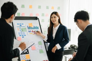 The boss stands near the board with graphs, demonstrates statistics, various personnel attending the training, introduces the new products of the company, in modern office