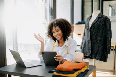 African tailor woman working on clothes in tailoring atelier.  beautiful young female fashion designer smile and after success in studio