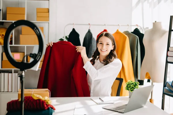 Fashion blogger concept, Young woman selling clothes on video streaming.Startup small business SME, using smartphone taking receive and checking in studio