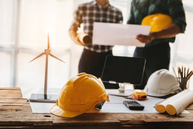 İnşaat ekibi ve miğferlerin arkasındaki yeni proje planı inşaat projeleri hakkında danışmanlık yapmak için ofis masasında. gün ışığında