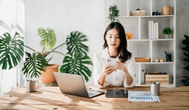  Çalışan kadın konsepti, video konferansına katılan Asyalı kadın yönetici ve ev ofisinde akıllı telefon ve bir fincan kahve.