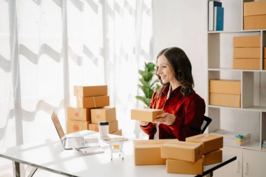 Başlangıçta küçük işletme KOBİ 'si, dizüstü bilgisayarı kullanan girişimci kadın paket ürün kutuları hazırlamak için online alışveriş siparişlerini alıp kontrol ediyor. ev ofisinde.