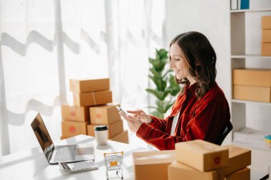 Başlangıçta küçük işletme KOBİ 'si, dizüstü bilgisayarı kullanan girişimci kadın paket ürün kutuları hazırlamak için online alışveriş siparişlerini alıp kontrol ediyor. ev ofisinde.
