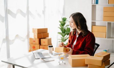 Başlangıçta küçük işletme KOBİ 'si, dizüstü bilgisayarı kullanan girişimci kadın paket ürün kutuları hazırlamak için online alışveriş siparişlerini alıp kontrol ediyor. ev ofisinde.
