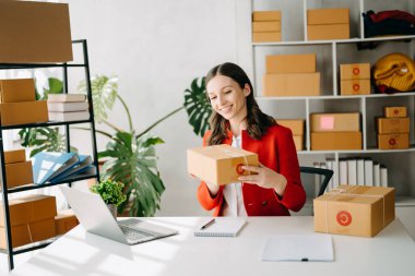 Başlangıçta küçük işletme KOBİ 'si, dizüstü bilgisayarı kullanan girişimci kadın paket ürün kutuları hazırlamak için online alışveriş siparişlerini alıp kontrol ediyor. ev ofisinde.