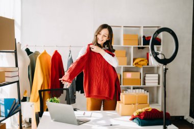 Beautiful lady blogger showing clothes in front of the camera to recording vlog video live streaming at her shop. Online Shopping Cart notion.