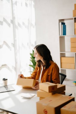 Başlangıçta küçük işletme KOBİ 'si, dizüstü bilgisayarı kullanan girişimci kadın paket ürün kutuları hazırlamak için online alışveriş siparişlerini alıp kontrol ediyor. ev ofisinde.