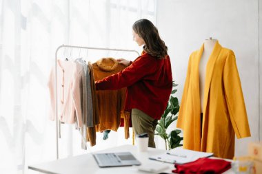Terzi kadın terzi atölyesinde giysiler üzerinde çalışıyor. Güzel genç bayan moda tasarımcısı gülümsemesi ve stüdyo başarısından sonra