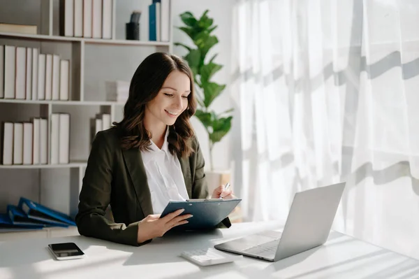 Confident business expert, attractive smiling young woman with laptop on desk in creative office.