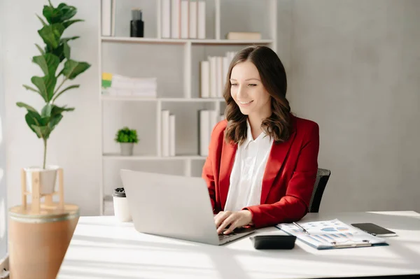 Confident business expert attractive smiling young woman typing laptop  on desk in creative office.