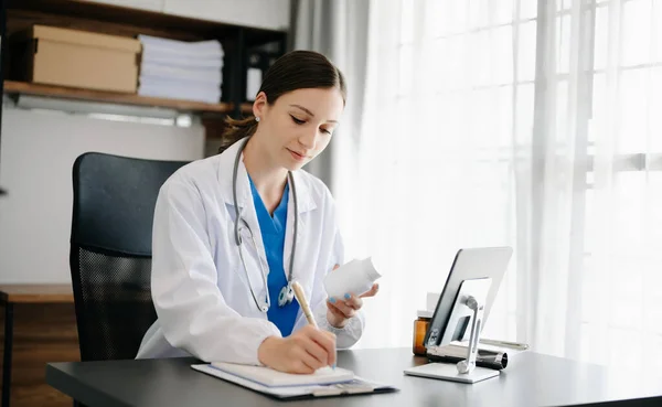 stock image Attractive female doctor talking while explaining medical treatment to patient through a video call with tablet pc in office