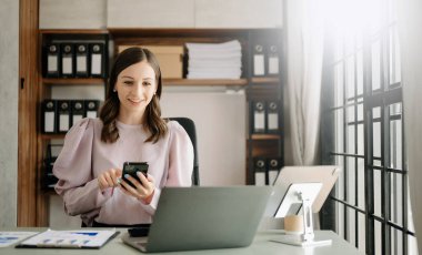 Yaratıcı ofiste dizüstü bilgisayarı ve telefonu olan kendine güvenen bir iş kadını.