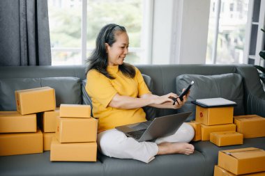 Başlangıçta küçük işletme KOBİ 'si, dizüstü bilgisayar kullanan girişimci sahibi Kıdemli Kadın paket ürün kutularını hazırlamak için online alışveriş siparişlerini alır ve kontrol eder. ev ofisinde.