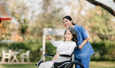 Asyalı yaşlı, yaşlı, yaşlı, tekerlekli sandalyede, Asyalı, dikkatli bir bakıcı ve bahçede yürüyen bir hastayı cesaretlendiren bir kadın. Bakıcının ve kıdemli sağlık sigortasının dikkatine.. 