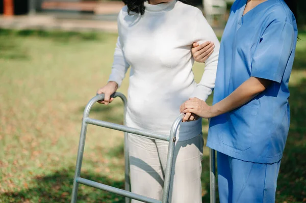 Asian careful caregiver or nurse and the happy patient  are walking in the garden to help and encourage and rest your mind with green nature. Help support yourself to learn to walk.