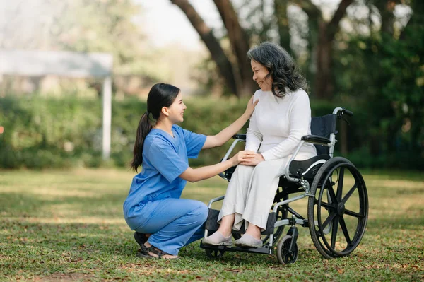 亚洲老年老年妇女坐在轮椅上 由亚洲小心照顾者照料 疗养院花园概念 — 图库照片