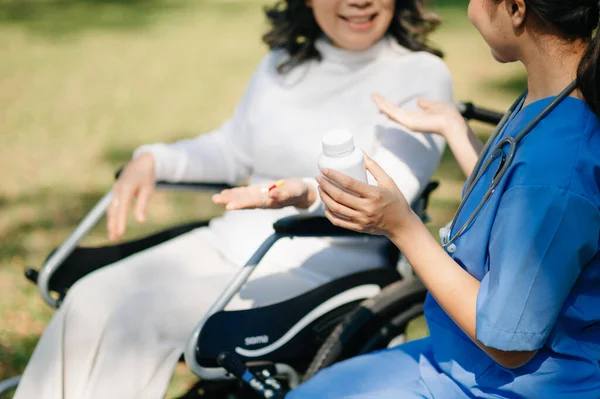 stock image Elderly asian senior woman on wheelchair with Asian careful caregiver and encourage patient, walking in garden. with care from a caregiver and senior health insurance. 