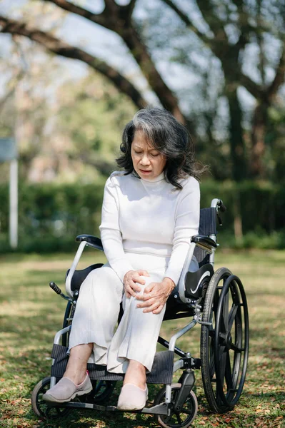 Asian old woman sitting on a wheelchair outdoors in the park