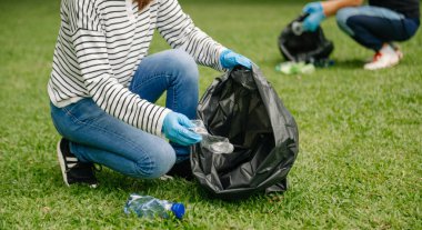 İki kişi parkta plastik şişeleri siyah torbalara koyuyor. Temizlik, kirlilik, ekoloji ve plastik konsept. 