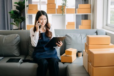 Genç işletme sahibi kadın, paket kutuları hazırla ve müşteriye teslimat için internetten siparişleri kontrol et. 