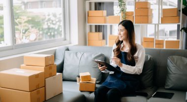Genç işletme sahibi kadın paket kutuları hazırlayın ve çevrimiçi alışveriş sitesi konseptine çevrimiçi teslimat için online siparişleri kontrol edin.