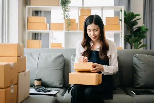 stock image Young business owner woman prepare parcel boxes and  check online orders for deliver to customer 