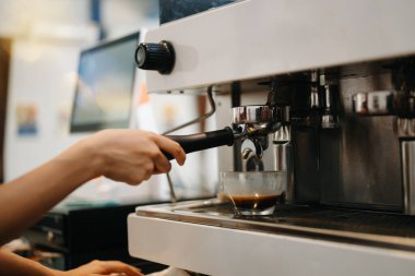 Eller ve profesyonel espresso makinesi cam bardağa taze kahve dolduruyor.