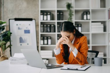 Asyalı kadın migren ağrısı çekiyor. Modern ofiste dizüstü bilgisayar üzerinde çalışırken çok çalışan iş kadını finansörü..