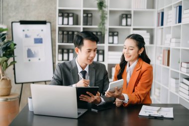 Asyalı iş adamları sunar ve açıklar ve dizüstü bilgisayar ve tablet kullanır. Takım çalışması, finansal pazarlama ekibi, modern ofis odasında otururken.