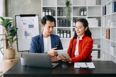 Asyalı iş adamları açıklama yapıyor ve dizüstü bilgisayar kullanıyor. Takım çalışması, finansal pazarlama ekibi, modern ofis odasında otururken.