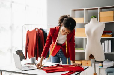Sakin, kıvırcık esmer, koyu tenli kadın modern moda tasarımcısı, dizüstü bilgisayar ve tablet bilgisayarın ofisinde.