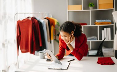 Genç iş sahibi Afrikalı kadın paket kutuları hazırlıyor ve çevrimiçi alışveriş konsepti olan tabletteki müşteriye teslim edilmesi için online olarak kontrol ediliyor..