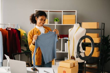 Moda blogcusu konsepti, genç Afrikalı kadın video yayınında kıyafet satıyor. Akıllı telefon ve dizüstü bilgisayar kullanarak küçük işletme KOBİ 'si kurun.